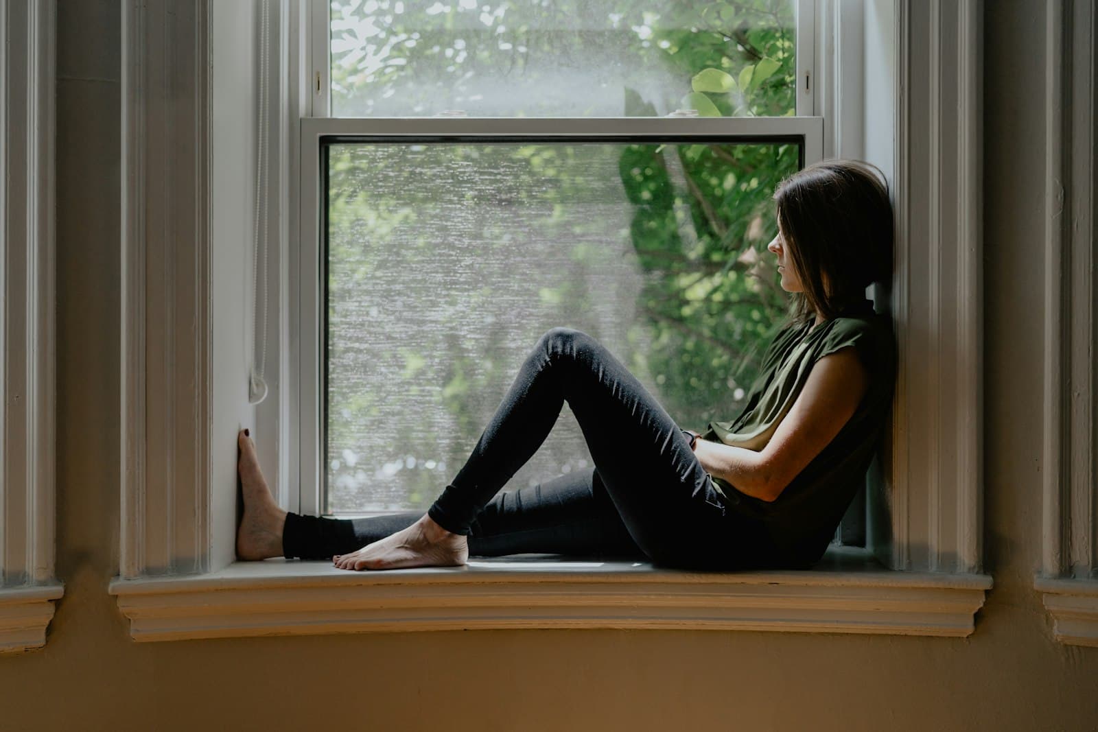 Eine Frau sitzt nachdenklich auf einer Fensterbank und schaut hinaus
