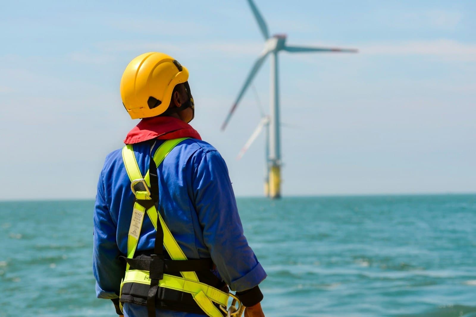 Ein Techniker mit Helm und Sicherungsgurt blickt auf eine Offshore-Windkraftanlage im Meer