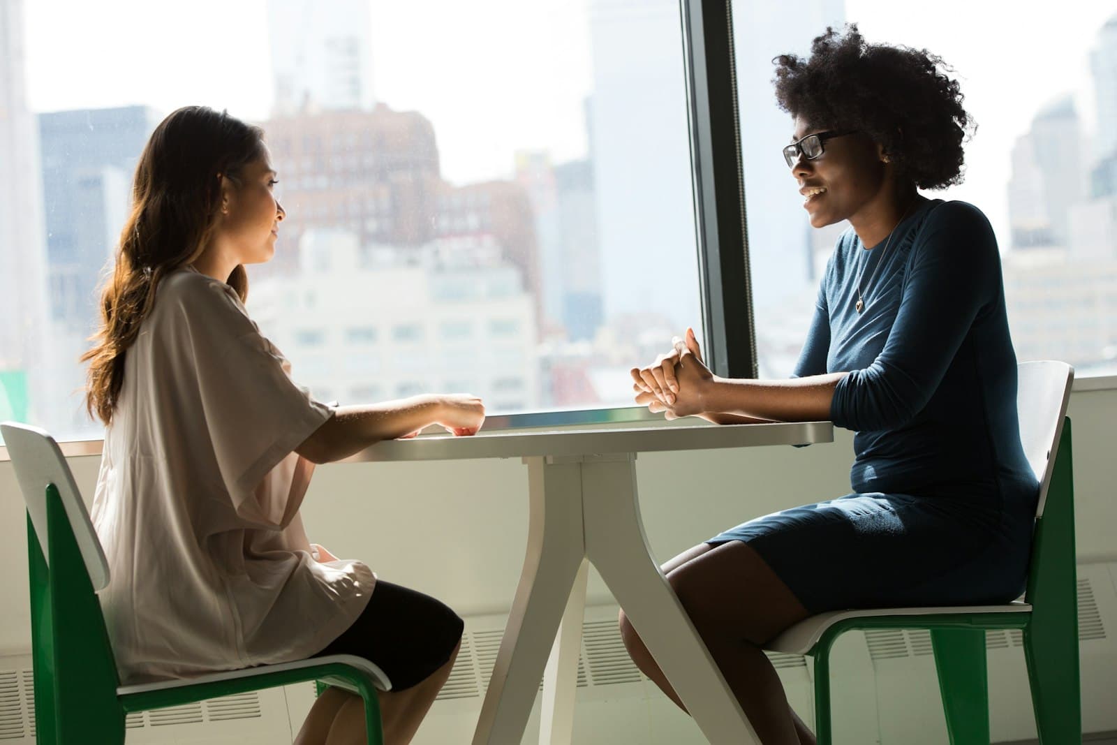 Zwei Frauen im Gespräch an einem Tisch vor einem großen Fenster
