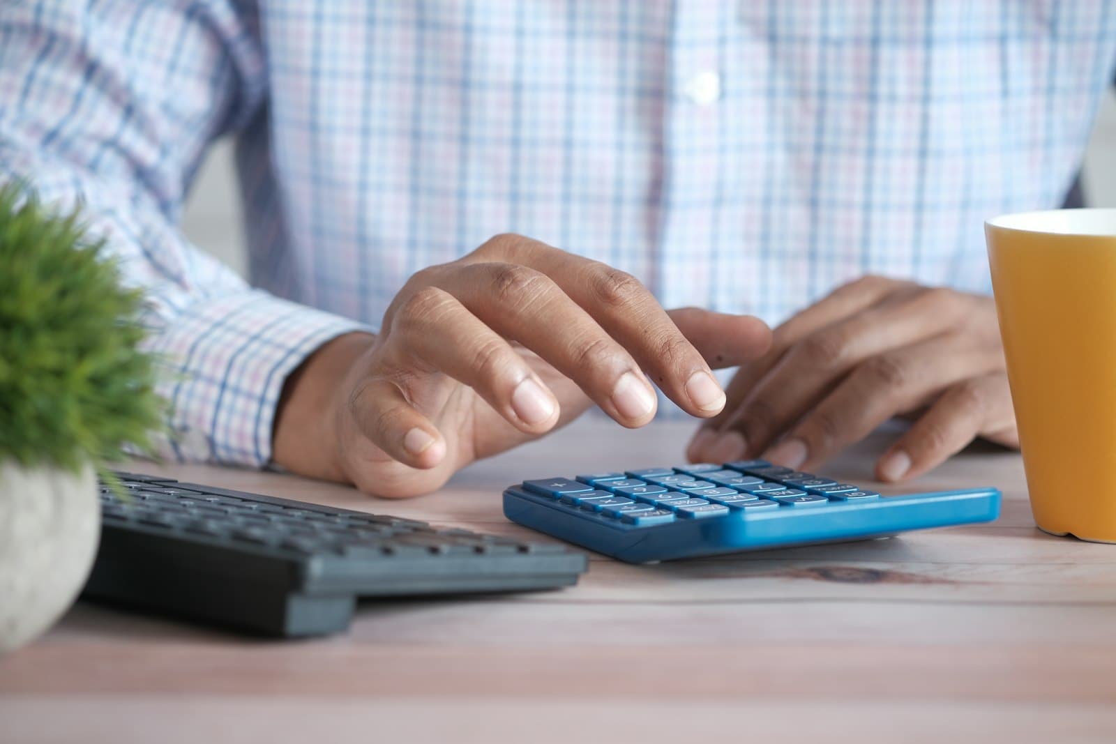Hände tippen auf einem Taschenrechner neben einer Tastatur