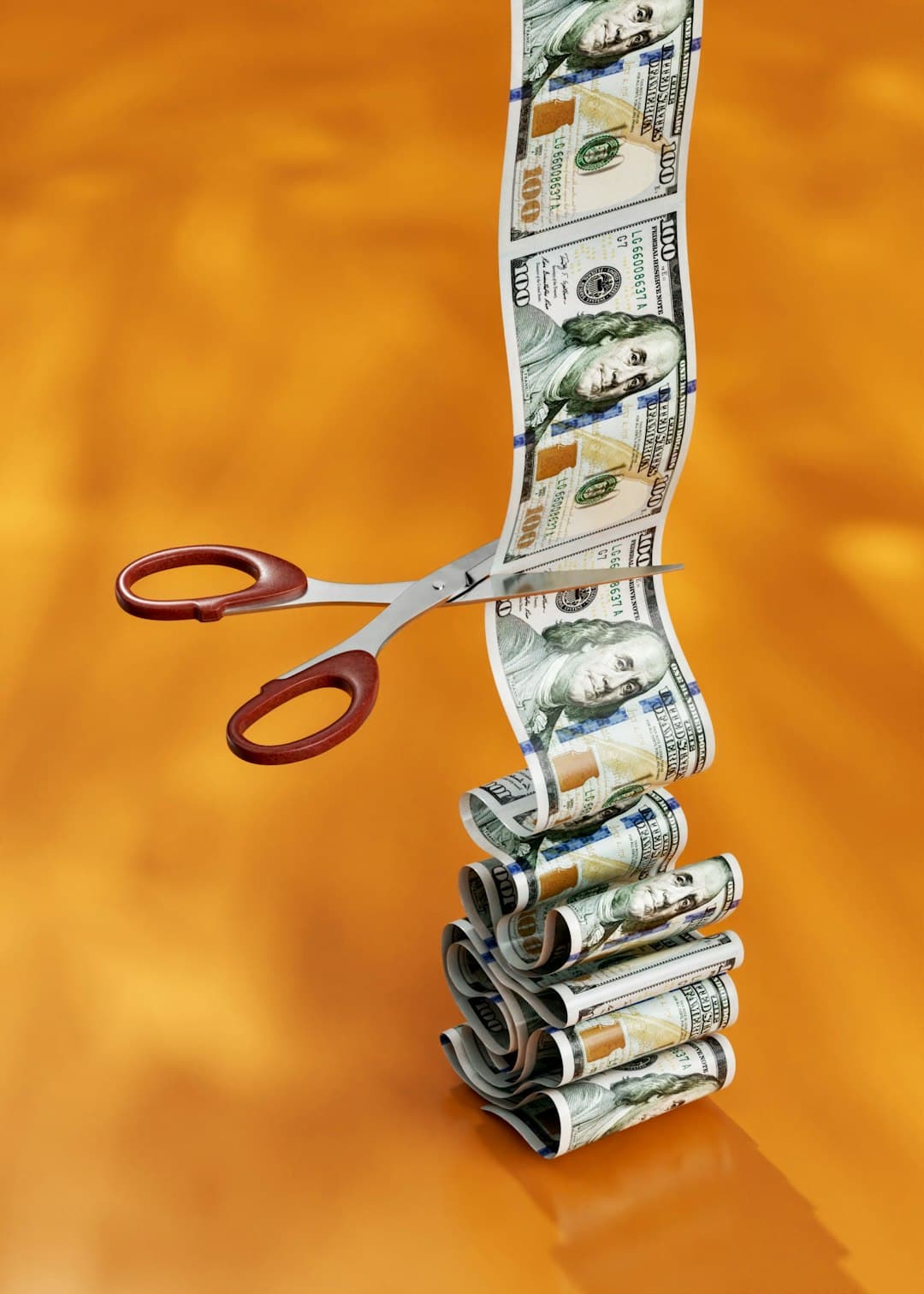 A pair of scissors cutting a continuous strip of one hundred dollar bills