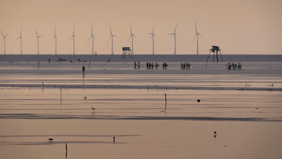 Wind turbines stand behind a vast expanse of water
