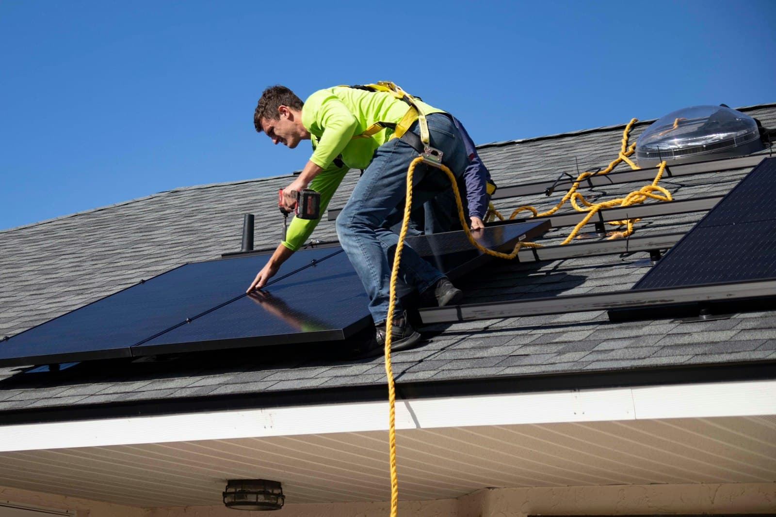 Ein Installateur mit Sicherungsseil montiert Solarmodule auf einem Hausdach