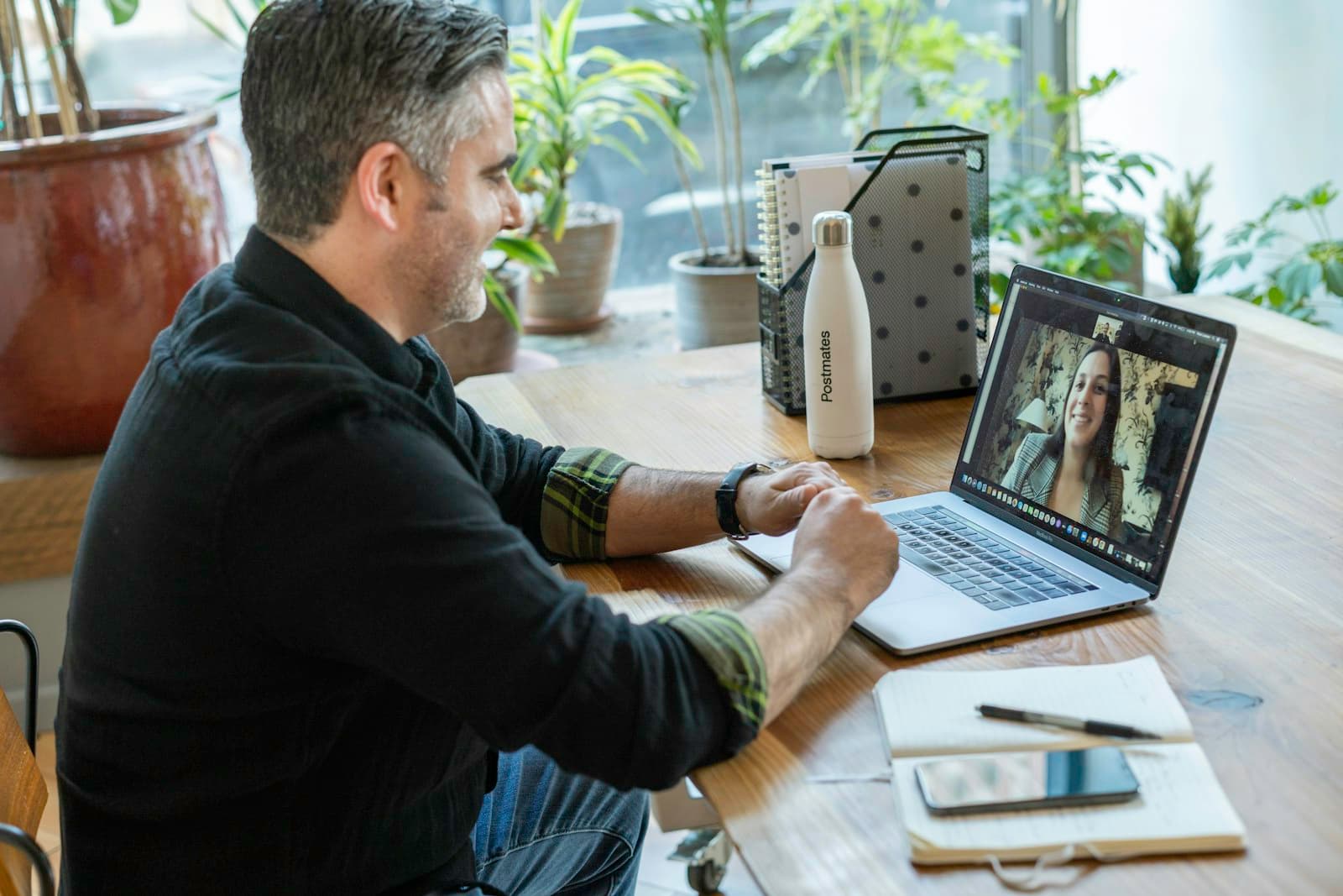 Ein Mann im Videocall am Laptop an einem Schreibtisch mit Pflanzen am Fenster