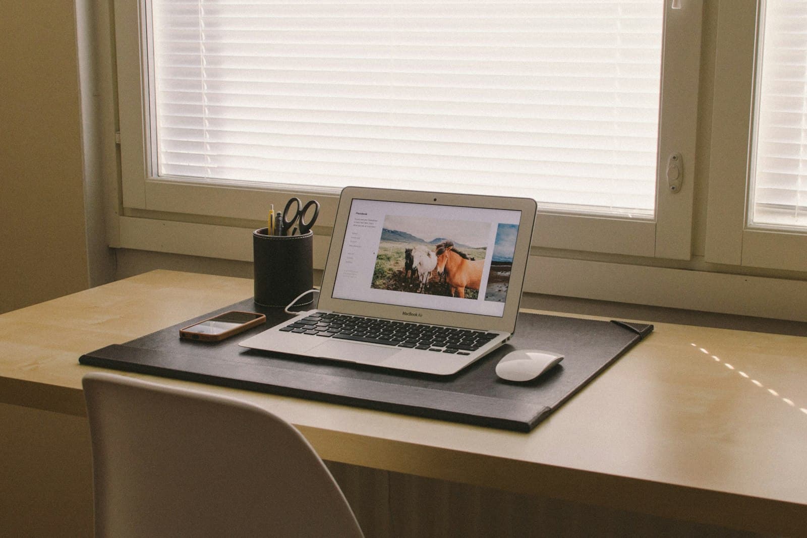 Laptop auf einem Holzschreibtisch am Fenster, Tageslicht fällt durch die Jalousie
