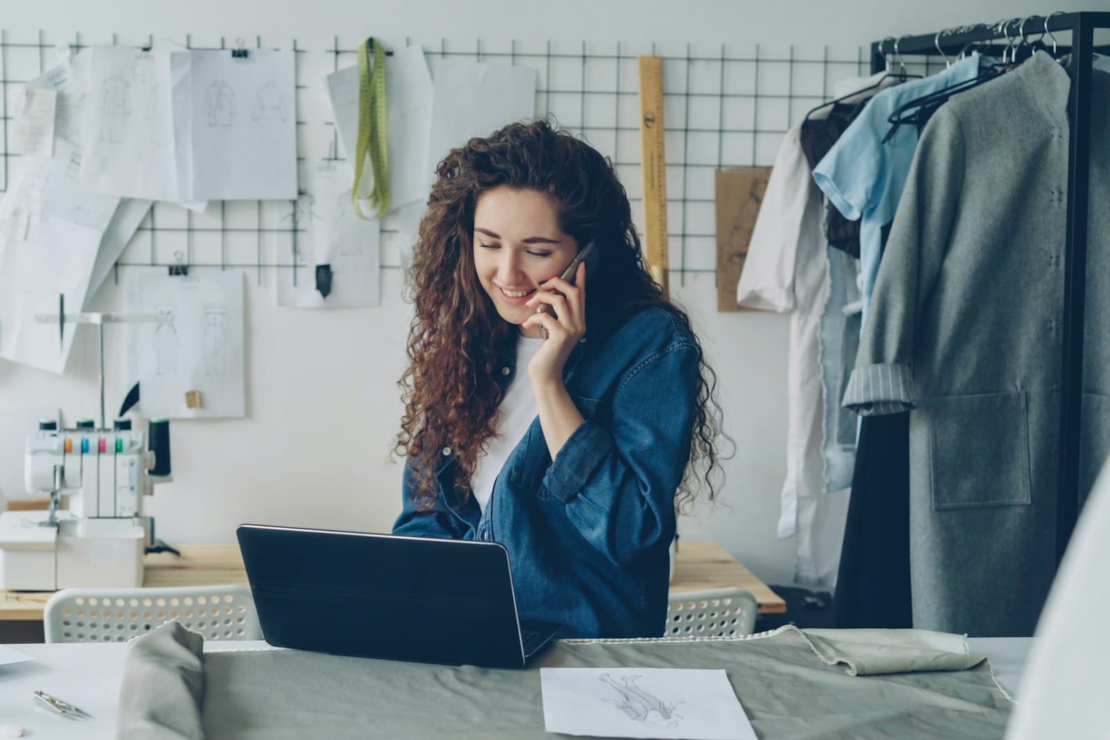 Eine Gründerin telefoniert in ihrem kleinen Modeatelier am Laptop