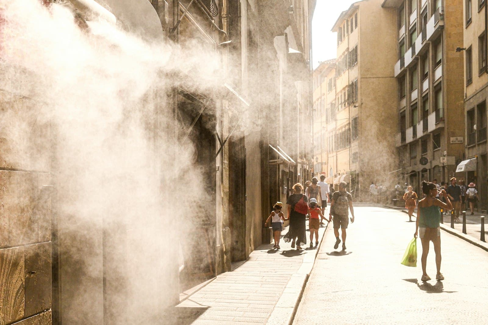 Sprühnebel kühlt eine sonnige Altstadtgasse, in der Menschen unterwegs sind